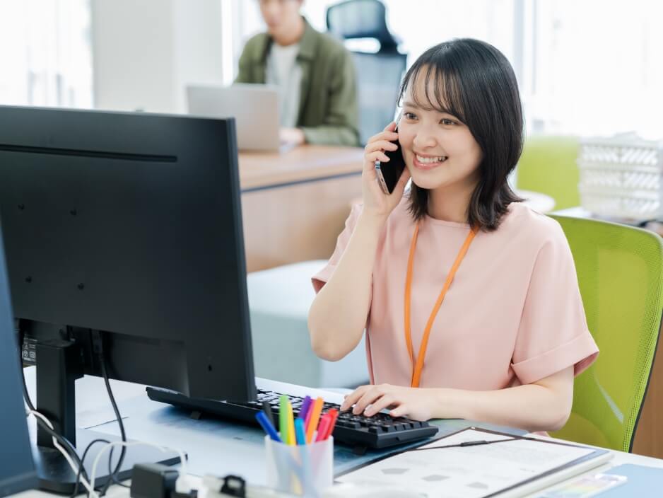 女性がデスクでパソコンを操作しながら電話応対する様子